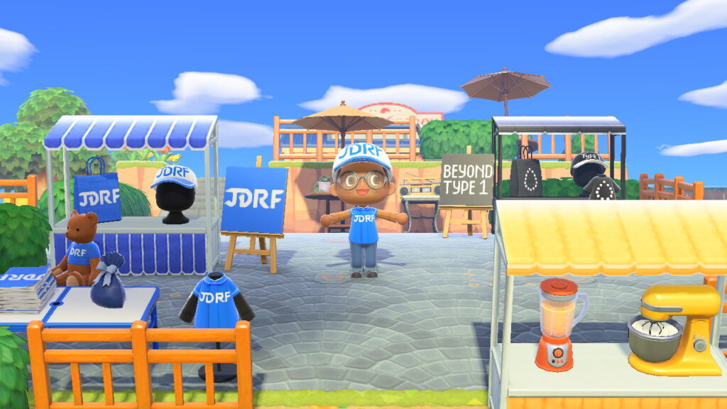 An Animal Crossing character wearing a JDRF cap, posing near a booth with JDRF merchandise and a teddy bear wearing a JDRF shirt.