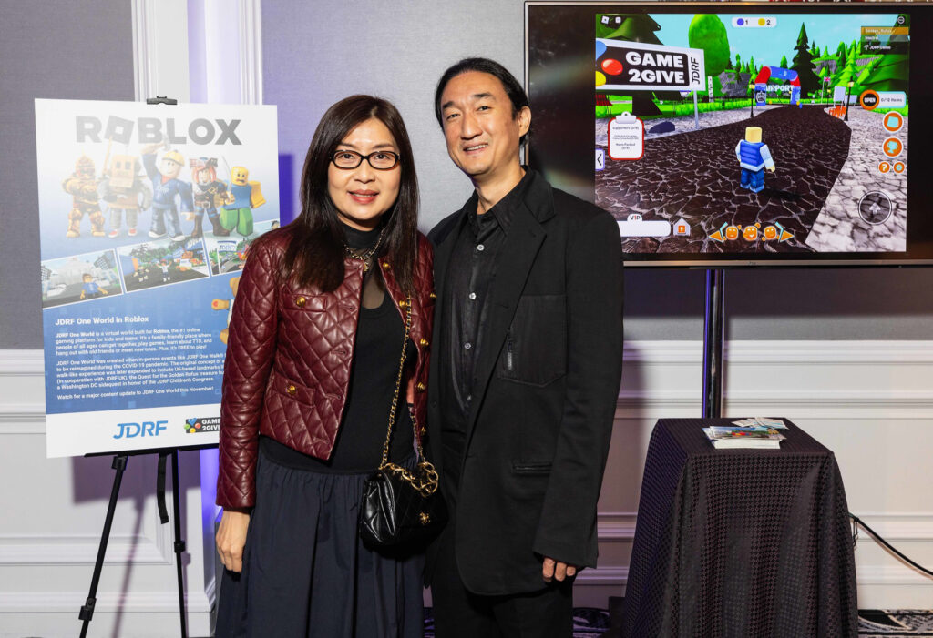 A couple in formal clothing standing in front of a Roblox poster and TV showing JDRF One World.